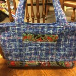 Blue fabric tote bag with multicolored patterned accents, sitting on a wooden table.