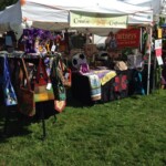 Craft fair stall displaying handbags, quilts, and chutney jars under a white tent on a grassy field.