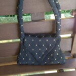 A black quilted handbag with a patterned design rests on a wooden bench.