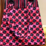 A tote bag with a geometric red and black pattern and black circular handles, placed on a wooden surface.