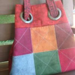 Colorful patchwork tote bag with metal ring handles on a wooden chair background.