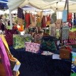 Outdoor market stall displaying colorful handmade bags on a table.