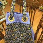 A floral-patterned tote bag with wooden ring handles sits on a wooden chair.
