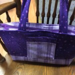 A purple fabric handbag with a patterned design hangs on a wooden chair.