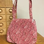 A red and white paisley pattern handbag sits on a wooden surface, next to a wooden drawer unit.