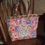 A colorful tote bag with house, cloud, and number patterns, placed on a wooden chair.
