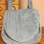 Blue textured fabric handbag with a flap, set on a wooden surface with a wooden cabinet in the background.