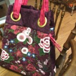 A floral-patterned tote bag with red handles hangs on a wooden chair.