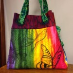 Colorful fabric tote bag with butterfly patterns and green handles, placed on a wooden surface.