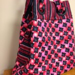 A colorful, patterned fabric tote bag with a geometric design and striped detailing, resting on a wooden surface.