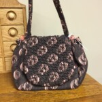 A black and pink patterned handbag with a scrunched design is placed on a wooden surface near a chest of drawers.