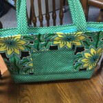 A large, green bag with yellow floral patterns, quilted texture, and sturdy handles rests on a wooden floor near a chair.