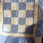 A blue and white patchwork quilt with floral patterns draped over a surface near a window.