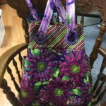 A colorful handbag with floral and striped patterns rests on a wooden chair.