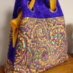 A colorful quilted handbag with vibrant spiral patterns and purple accents on a wooden surface.