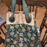 A floral patterned tote bag with large metal rings hangs on a wooden chair.
