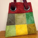A patchwork tote bag with red handles and six colored squares: brown, green, lime, yellow, and olive, on a wooden surface.