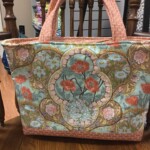 A floral-patterned tote bag with pink, blue, and green designs rests on a wooden chair.