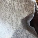 A quilt with abstract swirl patterns lies draped over a dark surface near a window.