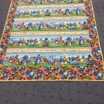 Colorful quilt with animal-themed patterns and floral border, displayed on a gray carpet.