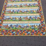 Colorful quilt with animal-themed patterns and floral border, displayed on a gray carpet.