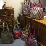 A collection of six colorful handbags displayed on and around wooden furniture in a carpeted room.
