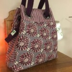 Purple and beige floral-patterned handbag with dark handles on a wooden surface.