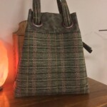A green and brown woven handbag with two round handles, placed on a wooden surface.