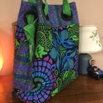 Colorful tote bag with green handles featuring blue, purple, and green abstract patterns, displayed on a wooden table.