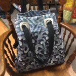 A fabric tote bag with a blue and white leaf pattern is hanging on a wooden rocking chair.