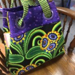 Colorful tote bag with green, purple, and multicolored floral patterns, resting on a wooden chair.