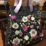 A floral-patterned tote bag on a wooden chair, featuring pink and white flowers with purple handles and striped accents.