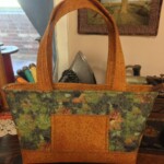 A handmade fabric tote bag with green, blue, and orange patterns is displayed on a wooden table.