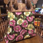 Floral-patterned handbag with textured brown handles on a wooden chair.