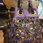 A floral-patterned tote bag with purple accents hangs on an intricately carved wooden chair.