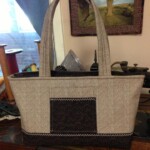 A handmade, textured tote bag with a black and gray pattern on a wooden surface, with sewing materials in the background.