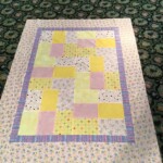 A colorful patchwork quilt with geometric patterns lies on a patterned green carpet.