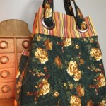 A large tote bag with floral and striped patterns is placed on a wooden surface next to a small wooden cabinet.