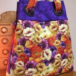 A colorful floral bag with large purple handles, featuring a bright pattern of purple, red, yellow, and orange flowers.