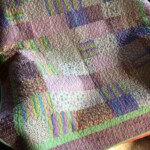 Colorful patchwork quilt with various patterned squares and a green border, illuminated by sunlight.