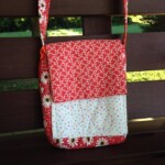 A red patterned shoulder bag with a floral design and polka dot flap rests on a wooden bench.