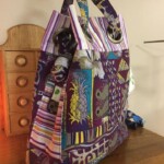 Colorful tote bag with a patchwork design featuring stripes, pineapples, and abstract patterns, placed on a wooden surface.