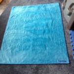 A blue quilt with floral patterns and "Tomás" written in the corner, laid on a gray carpet.