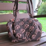 Brown and black patterned handbag with ruched detailing on a wooden bench outdoors.