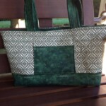 Green and white patterned tote bag with dual handles, displayed on a wooden bench.
