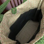 Green fabric tote bag with a patterned interior, featuring circular designs and a label near the opening.