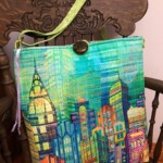 Colorful cityscape-themed shoulder bag with a green strap on an ornate wooden chair.