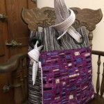 Colorful woven tote with a modern geometric design, featuring a knotted strap, resting on a wooden chair.