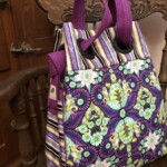 A purple and multicolored patterned tote bag with striped handles hangs on a wooden chair.