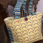 Colorful patterned tote bag with striped handles and a button closure on a wooden chair.